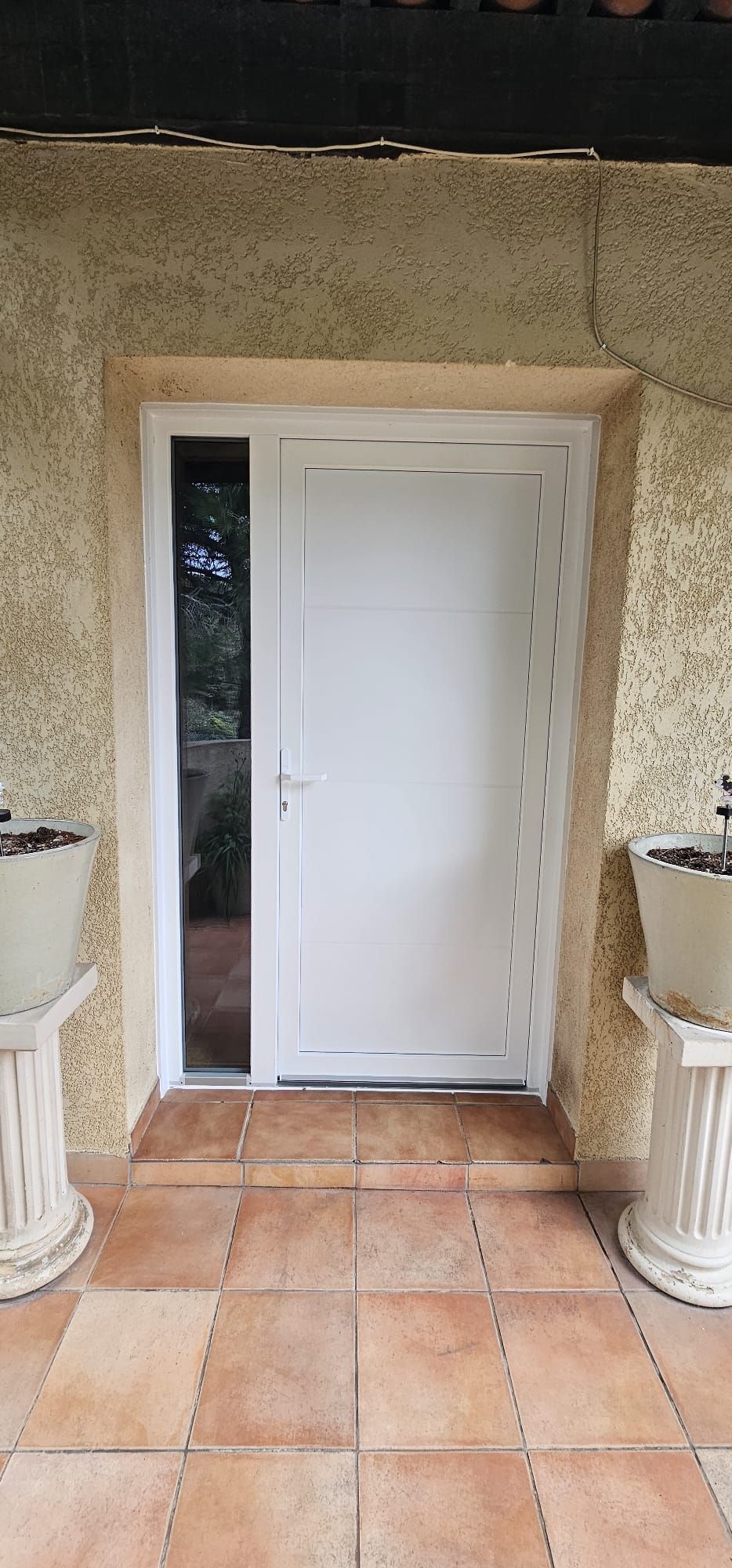 Porte blanche avec imposte latérale donnant sur une terrasse carrelée.