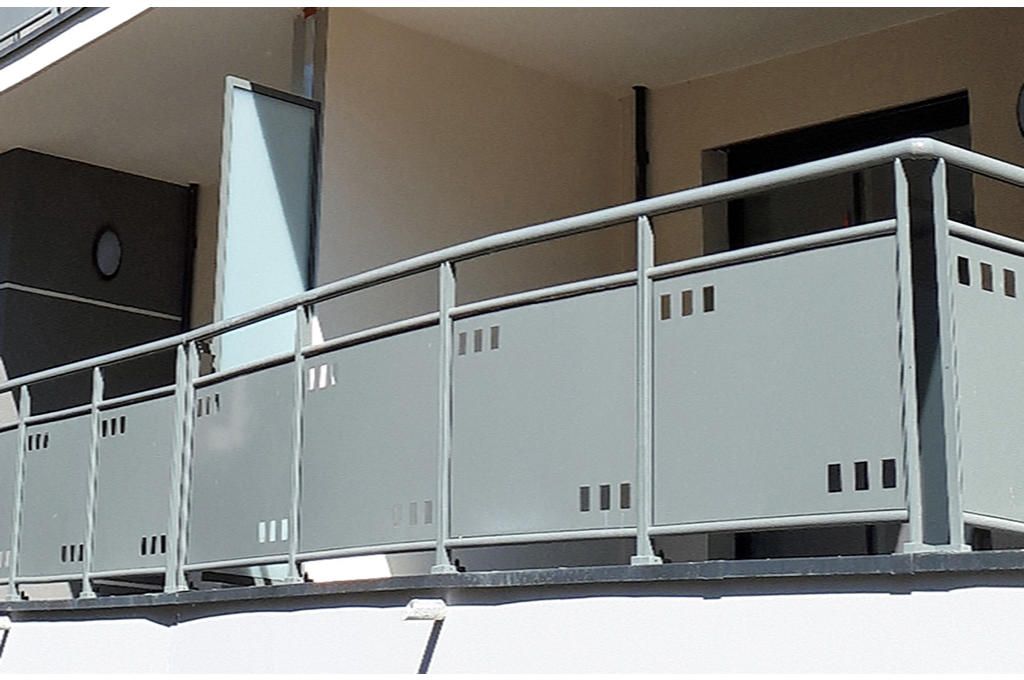 Rambarde rouge à l'extérieur d'un bâtiment, avec gravier et plantes.