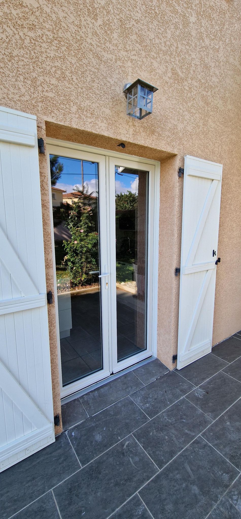 Portes-fenêtres blanches avec volets blancs, un nichoir fixé au mur au-dessus.