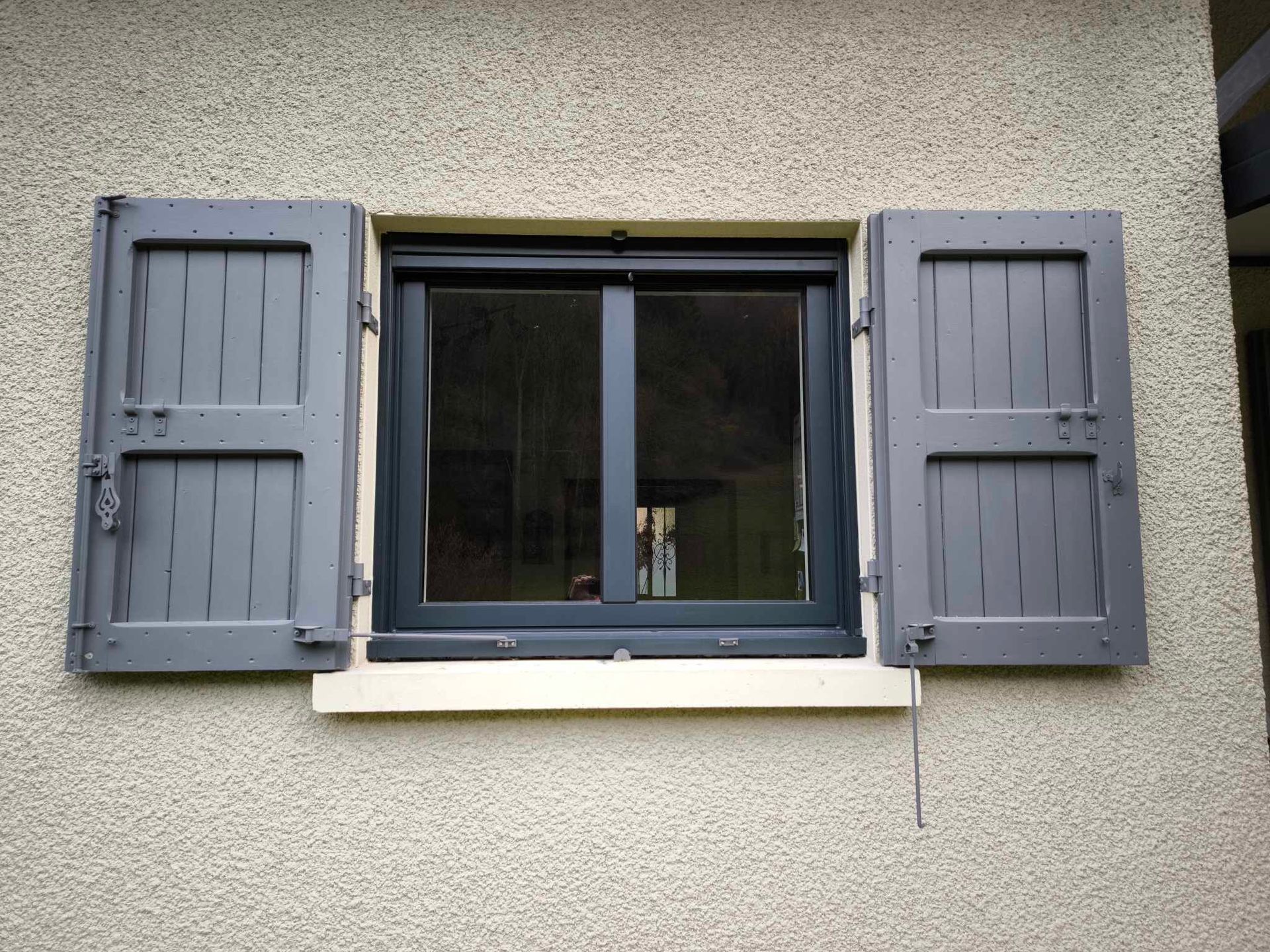 Fenêtre à volets gris ouverte sur un mur texturé.