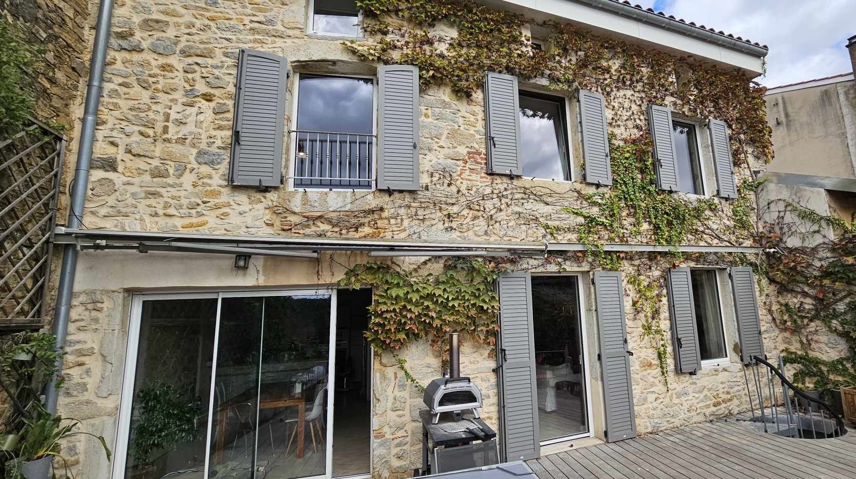 Maison en pierre avec des volets gris et des plantes grimpantes.