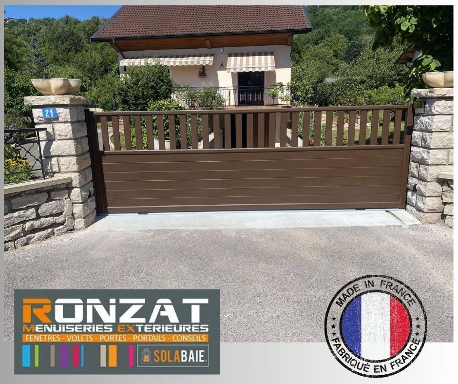 Portail coulissant marron devant une maison, encadré par des piliers en pierre.