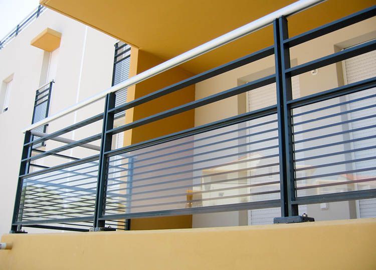 Rambarde de balcon en métal noir avec remplissage en fil métallique horizontal, sur un bâtiment aux accents jaunes.