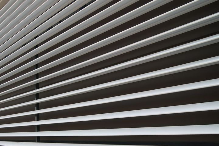 Stores horizontaux blancs inclinés sur une surface brun foncé.