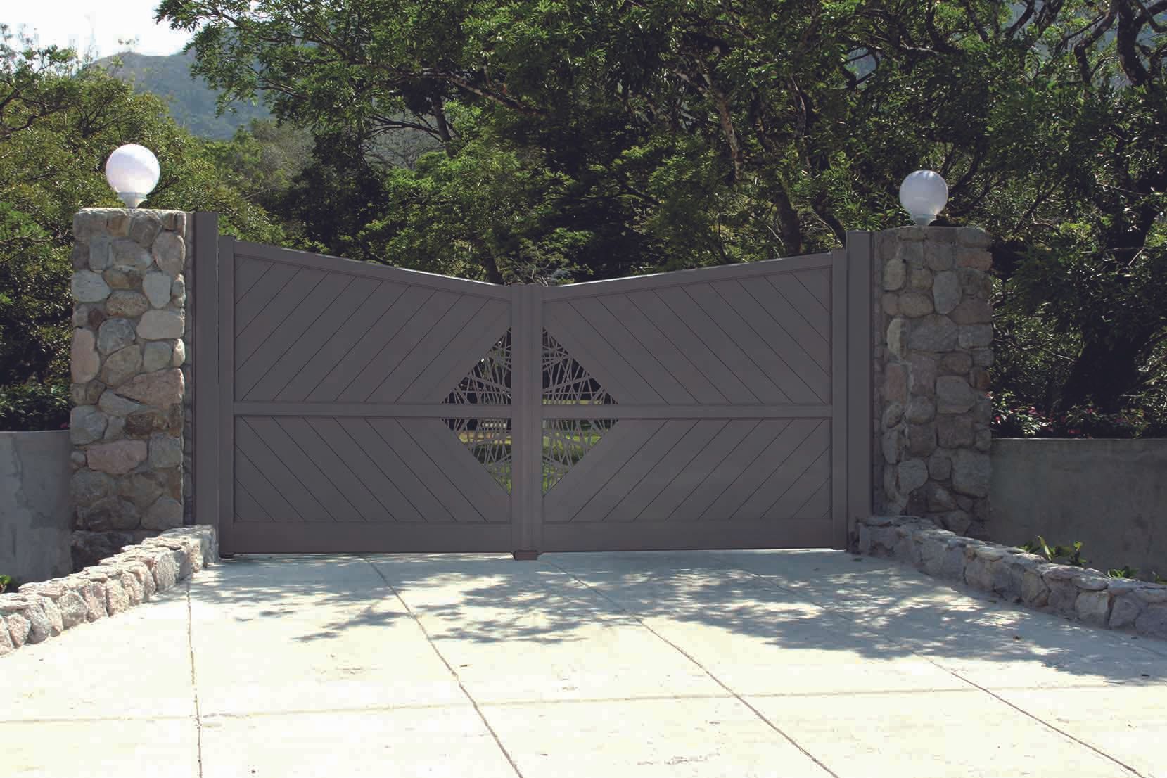 Portail en bois gris avec piliers en pierre, au design orné, donnant sur une allée carrossable.