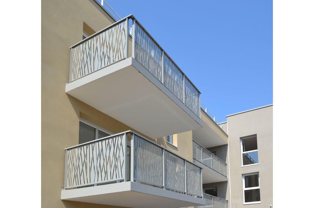 Balcons ornés de panneaux métalliques décoratifs sur un immeuble moderne, ciel bleu azur.