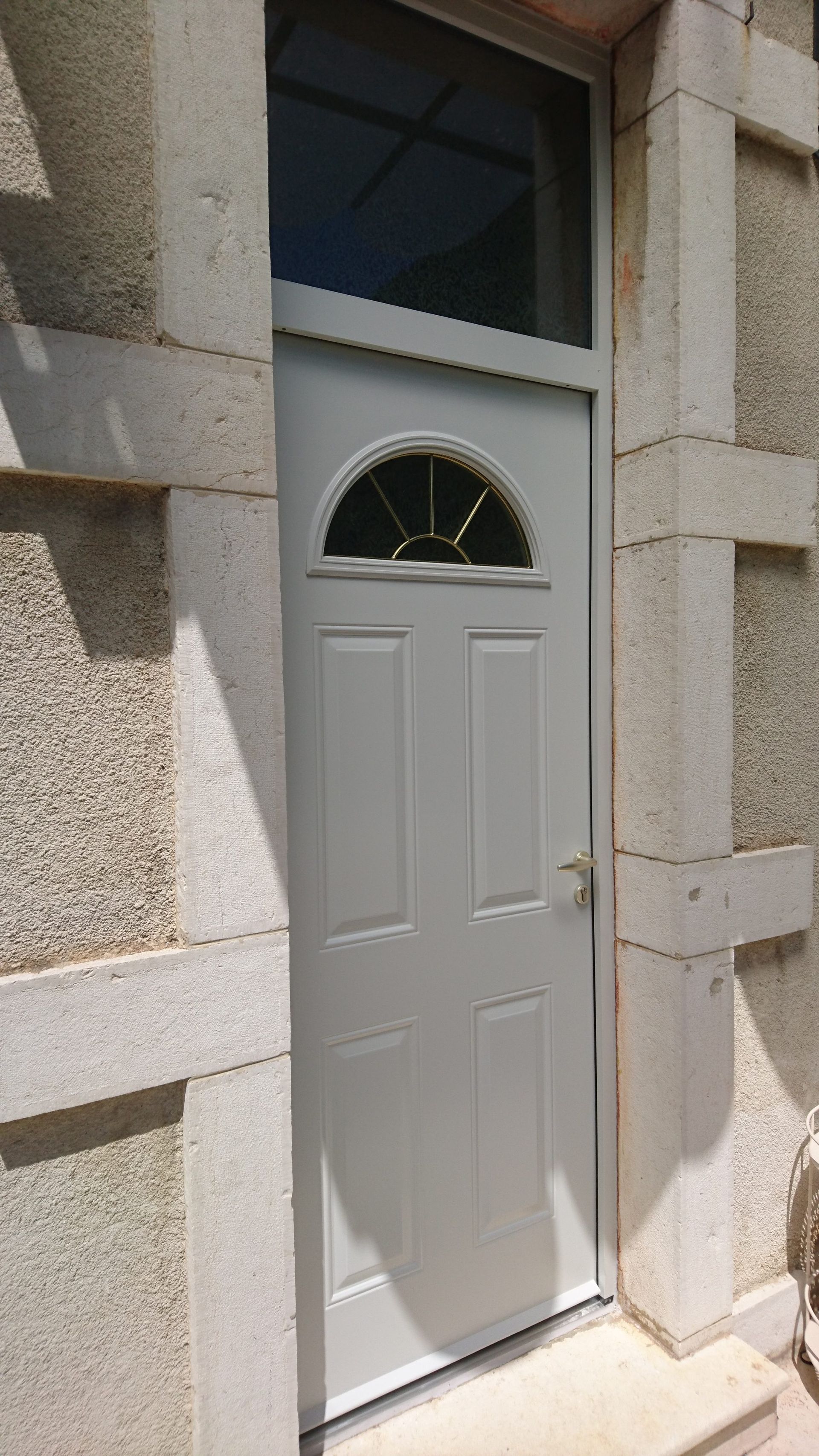 Porte d'entrée noire à motif géométrique, sous un porche orné de guirlandes lumineuses et d'une plante en pot.