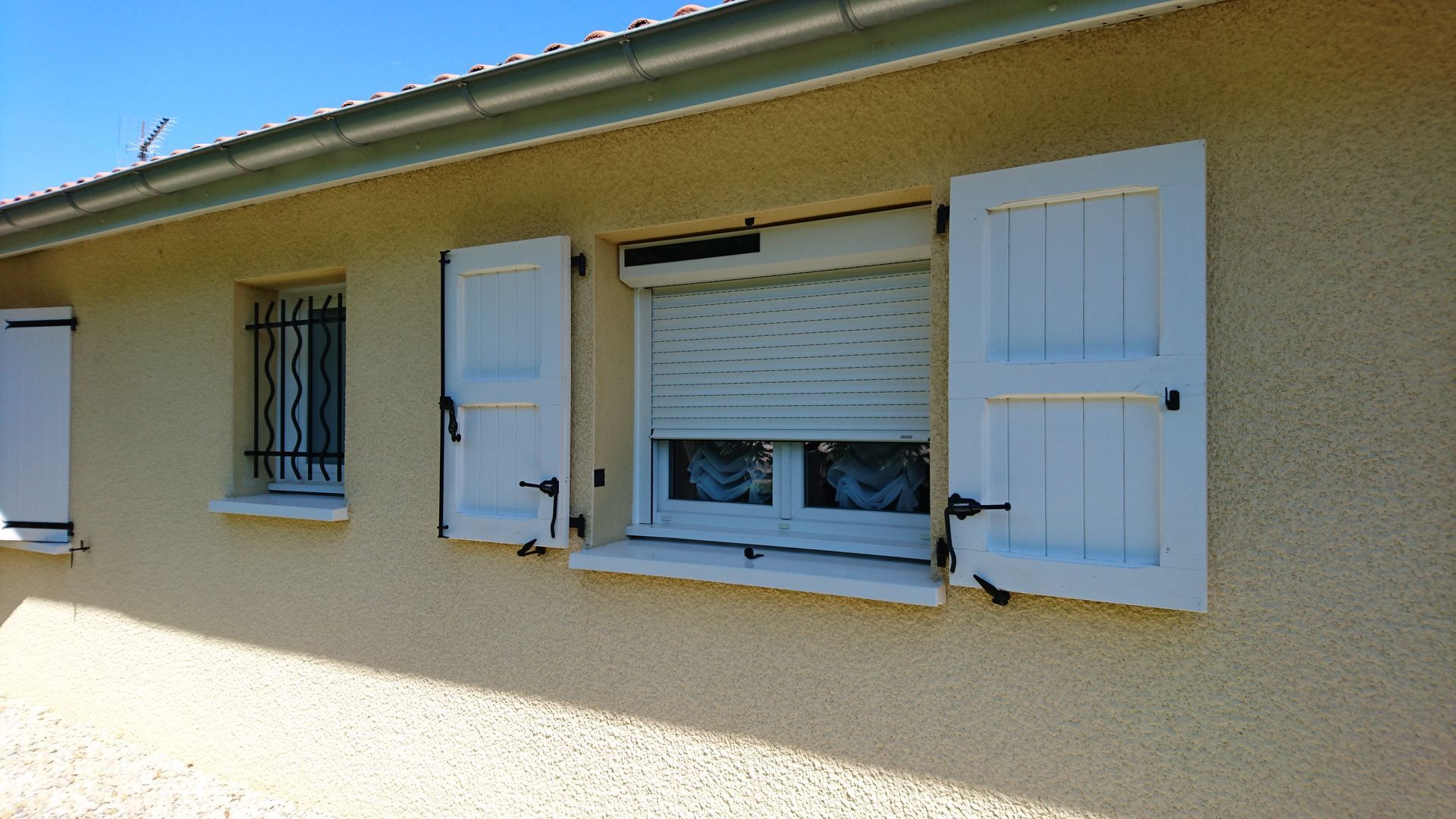 Extérieur d'un bâtiment avec des volets blancs, un volet roulant fermé et une fenêtre à barreaux.
