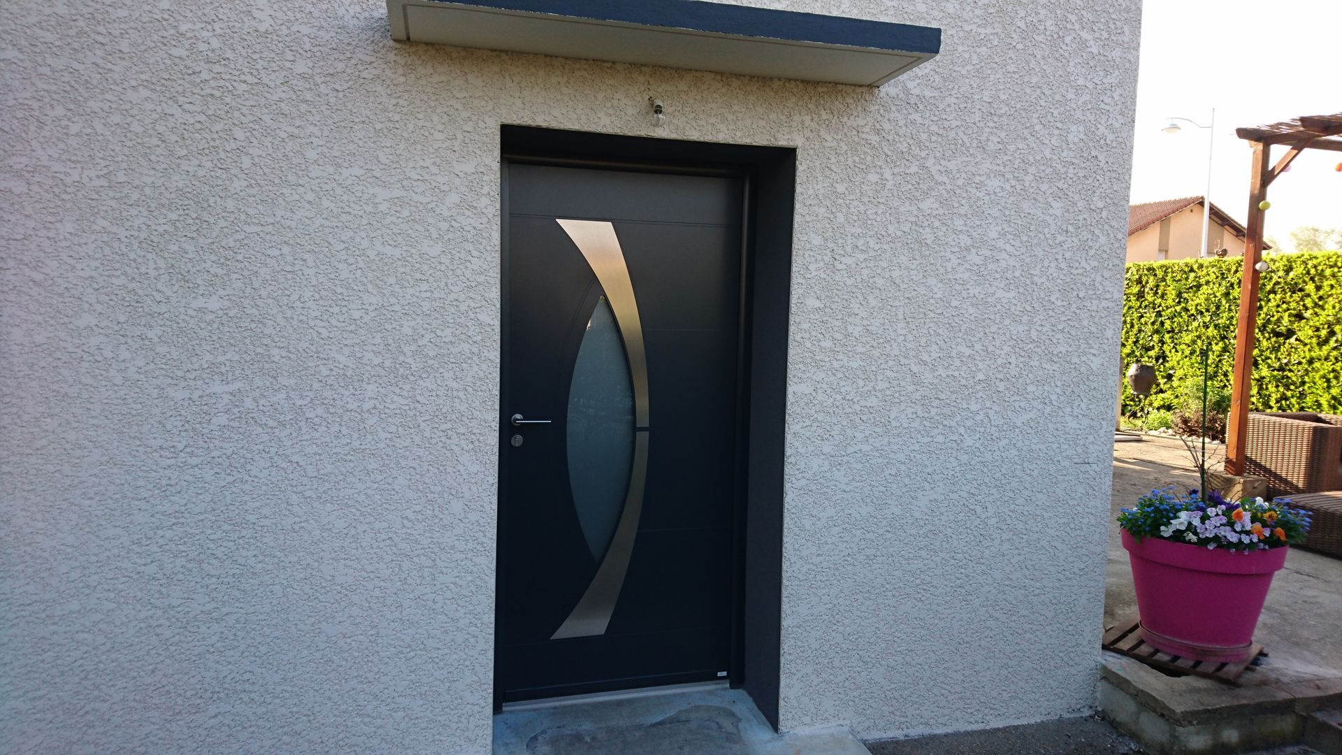 Porte d'entrée noire ornée de motifs dorés incurvés, sous un petit auvent, encastrée dans un mur en stuc.