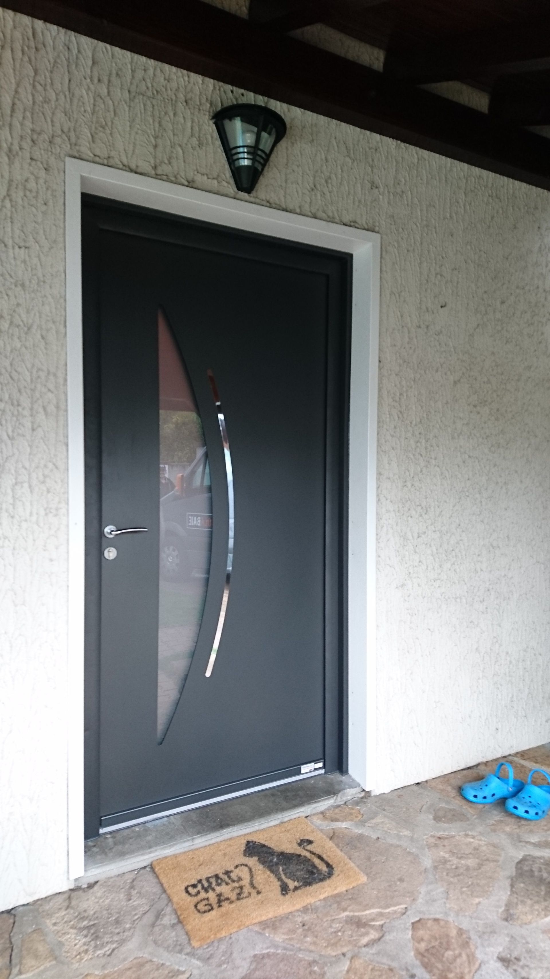 Porte d'entrée gris foncé avec panneau de verre incurvé, cadre blanc et paillasson de bienvenue « chat cool ».