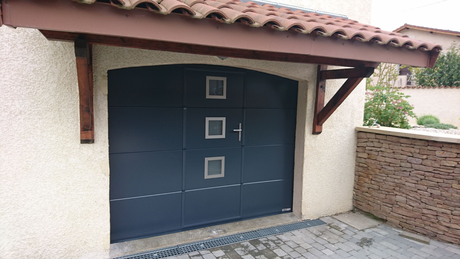 Gros plan sur un volet roulant fermé, de couleur claire, devant un bâtiment beige clair. Le cadre est gris foncé.