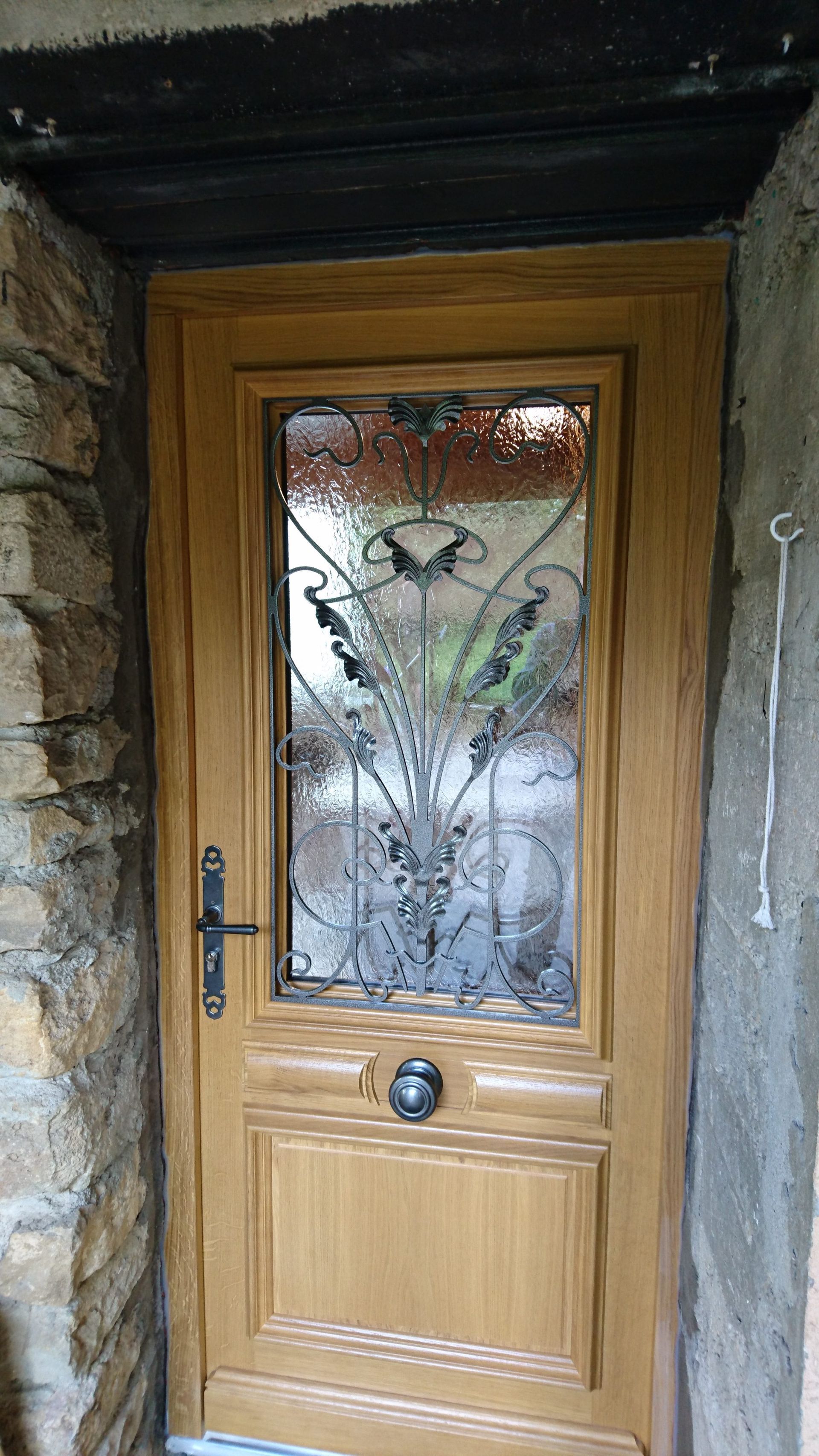 Porte d'entrée en bois avec panneau de verre décoratif et ferronnerie noire.