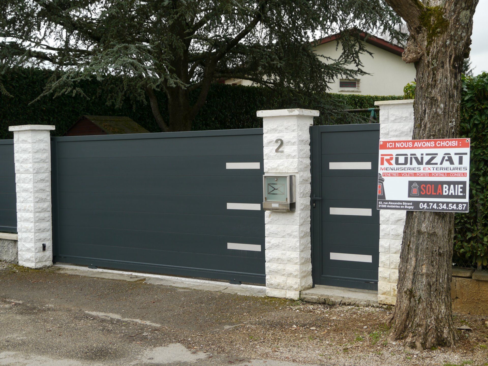 Portail coulissant marron devant une maison, encadré par des piliers en pierre. Il porte le sceau « Fabriqué en France ».