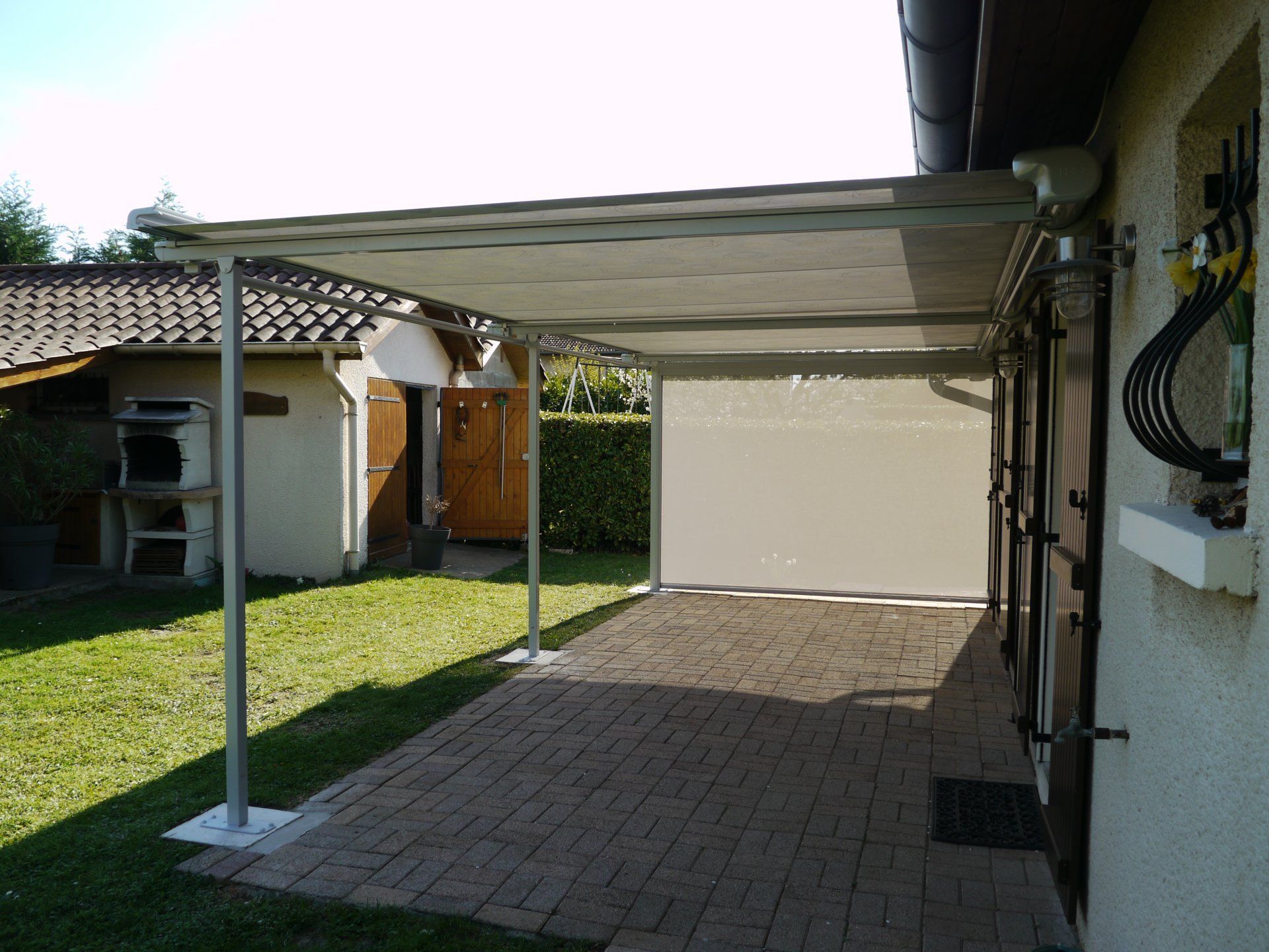 Abri voiture attenant à une maison avec terrasse en briques et jardin gazonné.