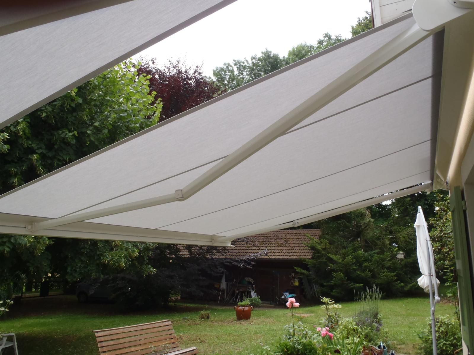 Un store rétractable blanc ombrage une pelouse et un jardin verdoyants.