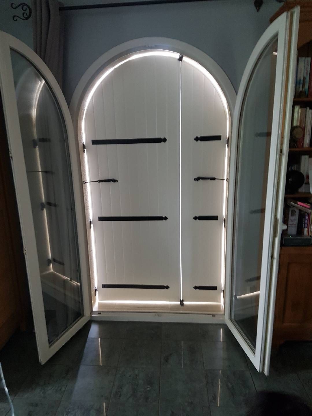 Fenêtre cintrée blanche avec portes ouvertes, révélant un volet blanc fermé.