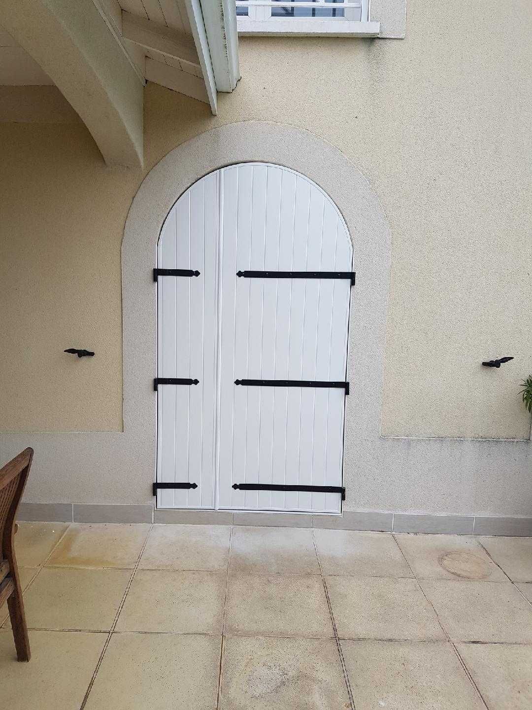 Porte cintrée en bois blanc avec quincaillerie noire, encastrée dans un mur en stuc beige clair sur un patio.