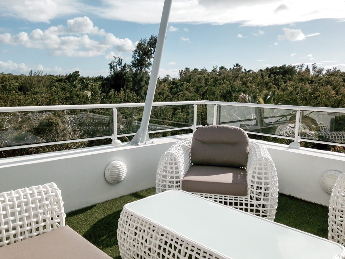 Mobilier de jardin blanc sur un toit-terrasse avec balustrade en verre, donnant sur les arbres et le ciel bleu.