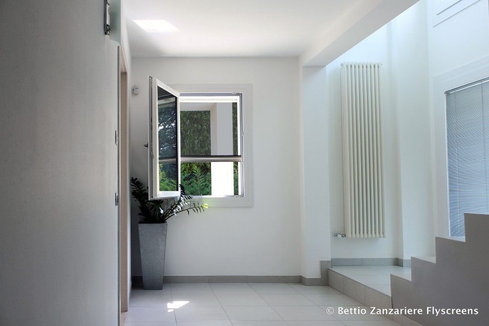 Couloir blanc avec fenêtre ouverte, radiateur et plante en pot.