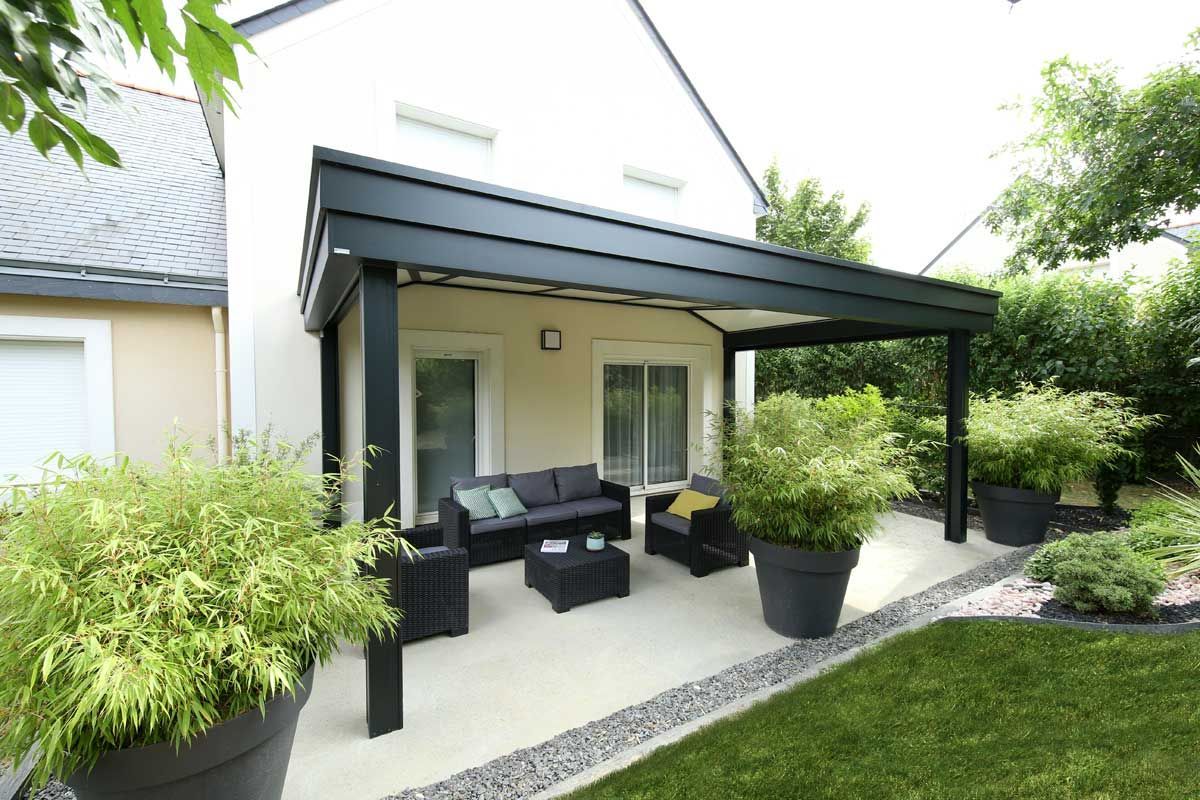 Terrasse avec auvent noir, mobilier de jardin, plantes en pot et pelouse verte.