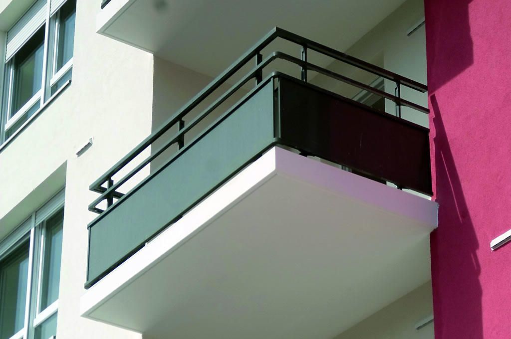 Balcon sur un immeuble moderne, en béton blanc avec rambarde foncée et panneau vert.
