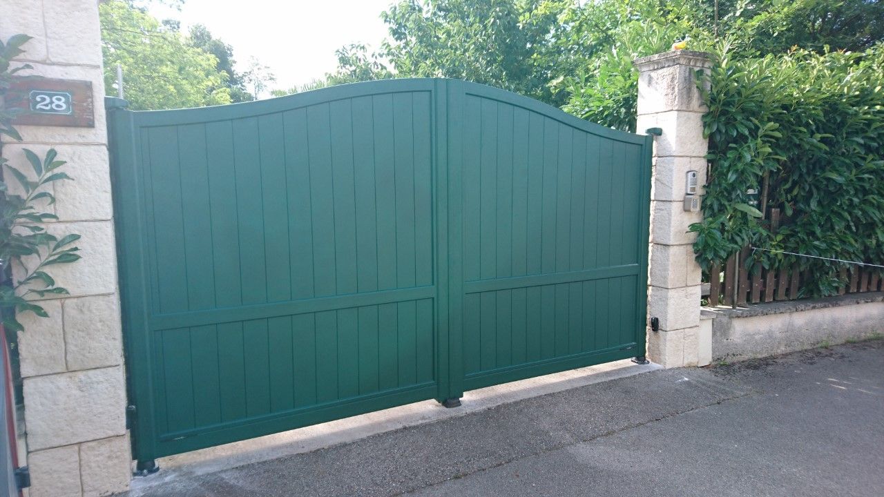 Portail vert à sommet arrondi, entre des piliers de pierre, bloquant une allée.