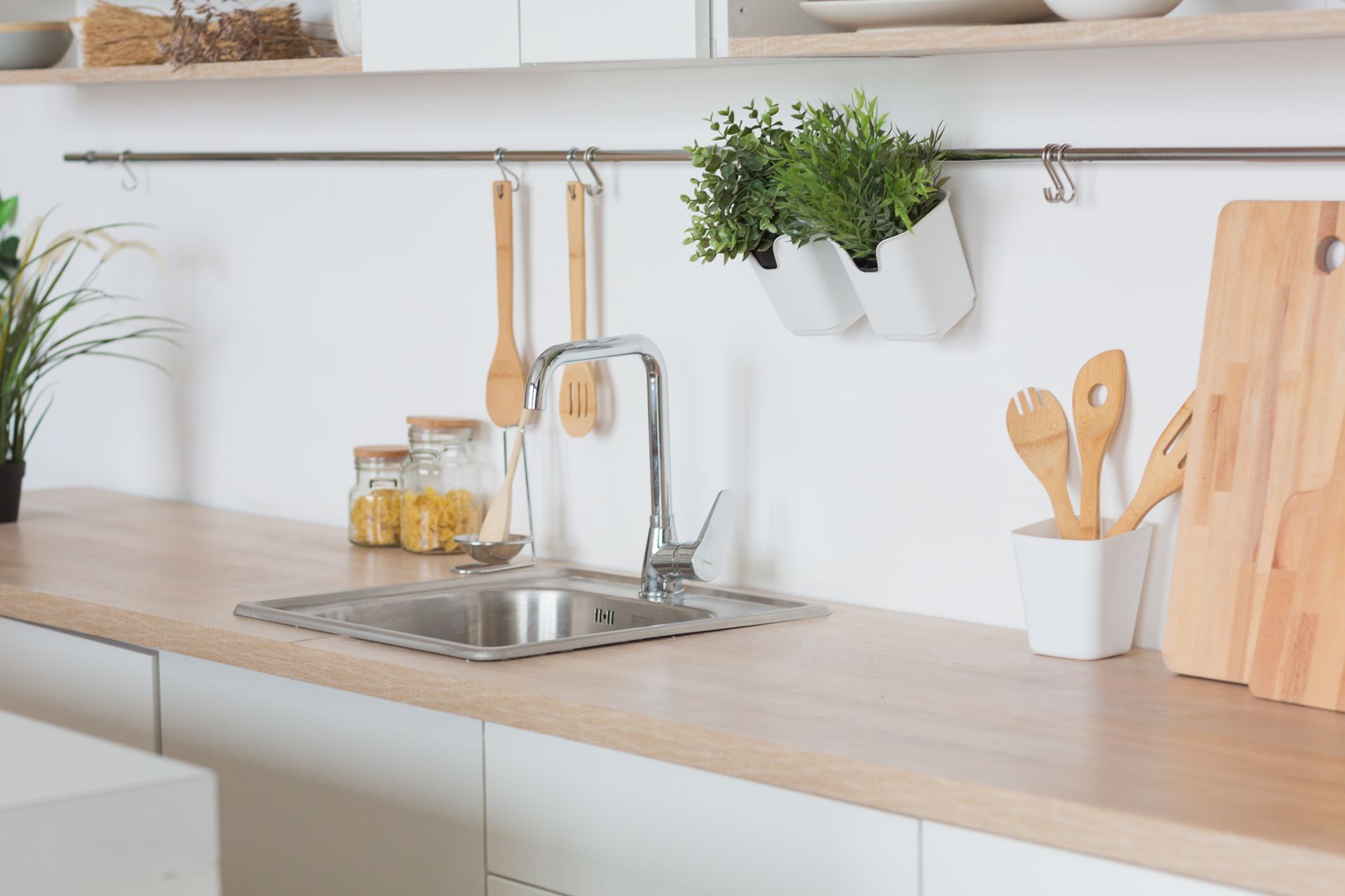 Un coin évier lumineux et moderne avec des plans de travail en bois, des ustensiles suspendus, une plante en pot et des planches à découper.