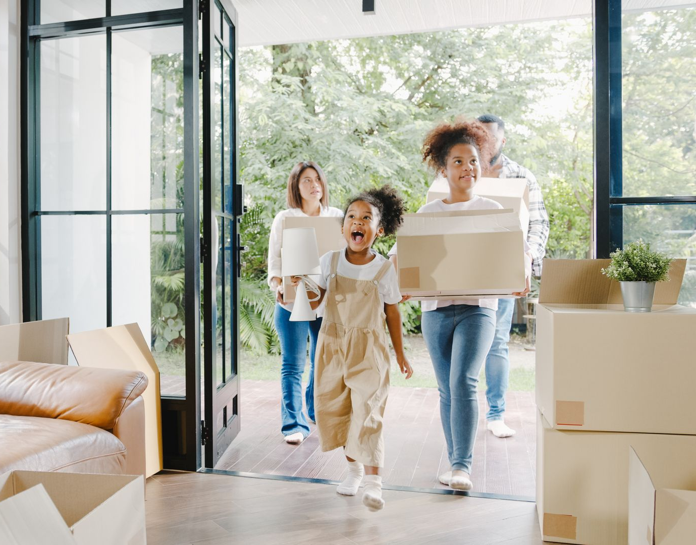 Une famille heureuse franchit une porte ouverte et entre dans sa nouvelle maison, portant des cartons de déménagement.
