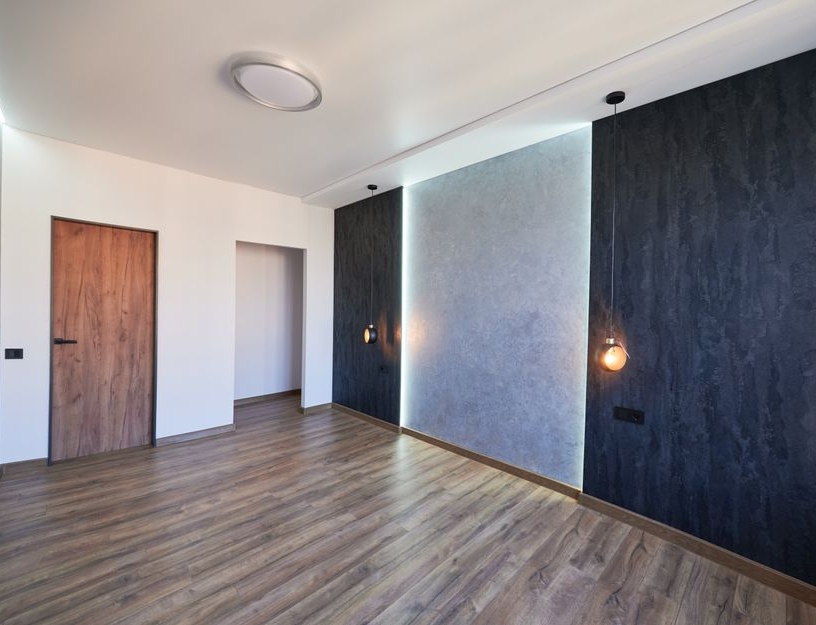 Une pièce moderne avec un sol imitation bois, une porte à grain de bois et un mur orné de panneaux sombres et d'un centre illuminé.
