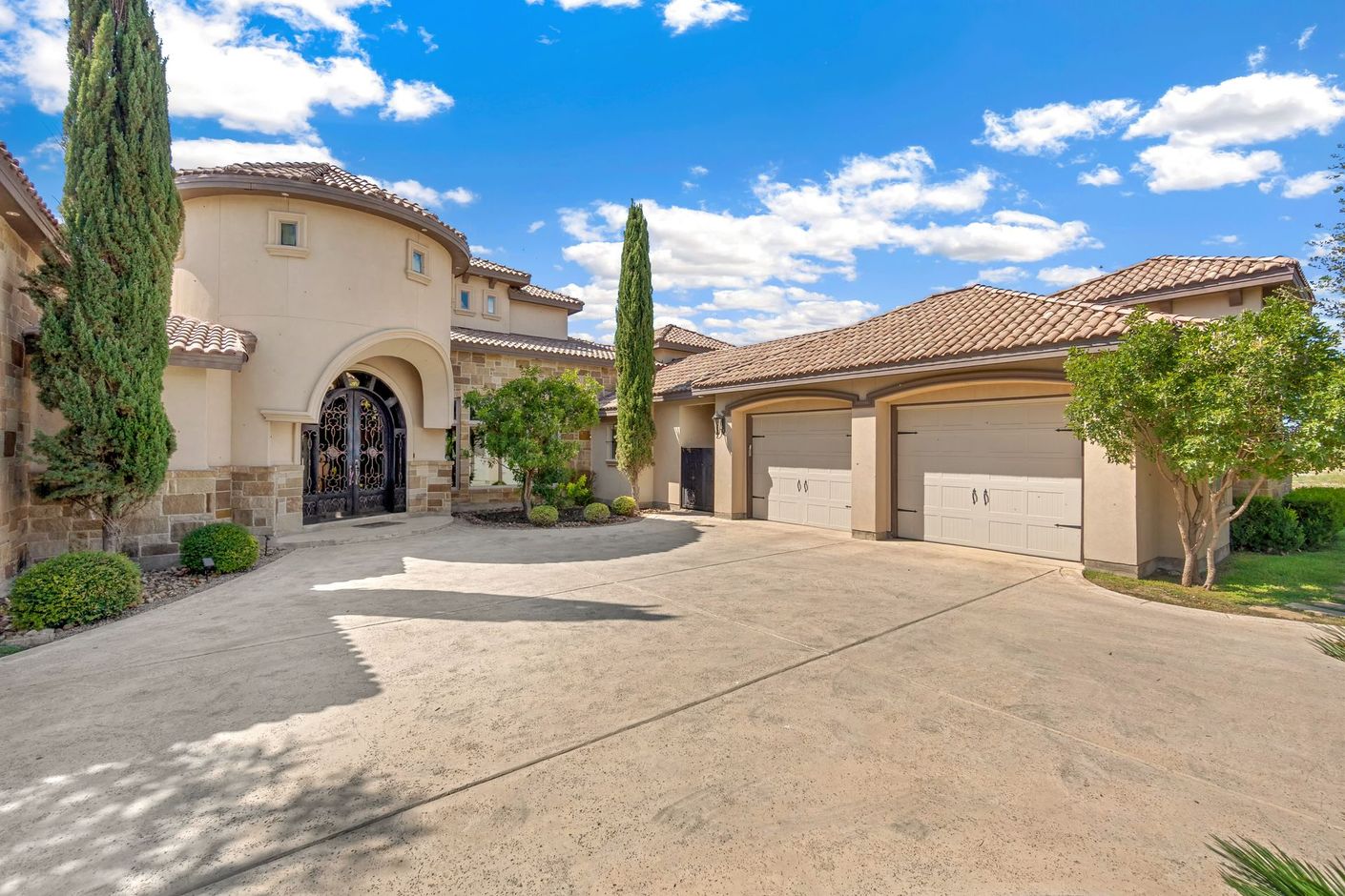 Une grande maison de style méditerranéen, en stuc beige, avec un toit de tuiles, un garage pour trois voitures et une allée circulaire.