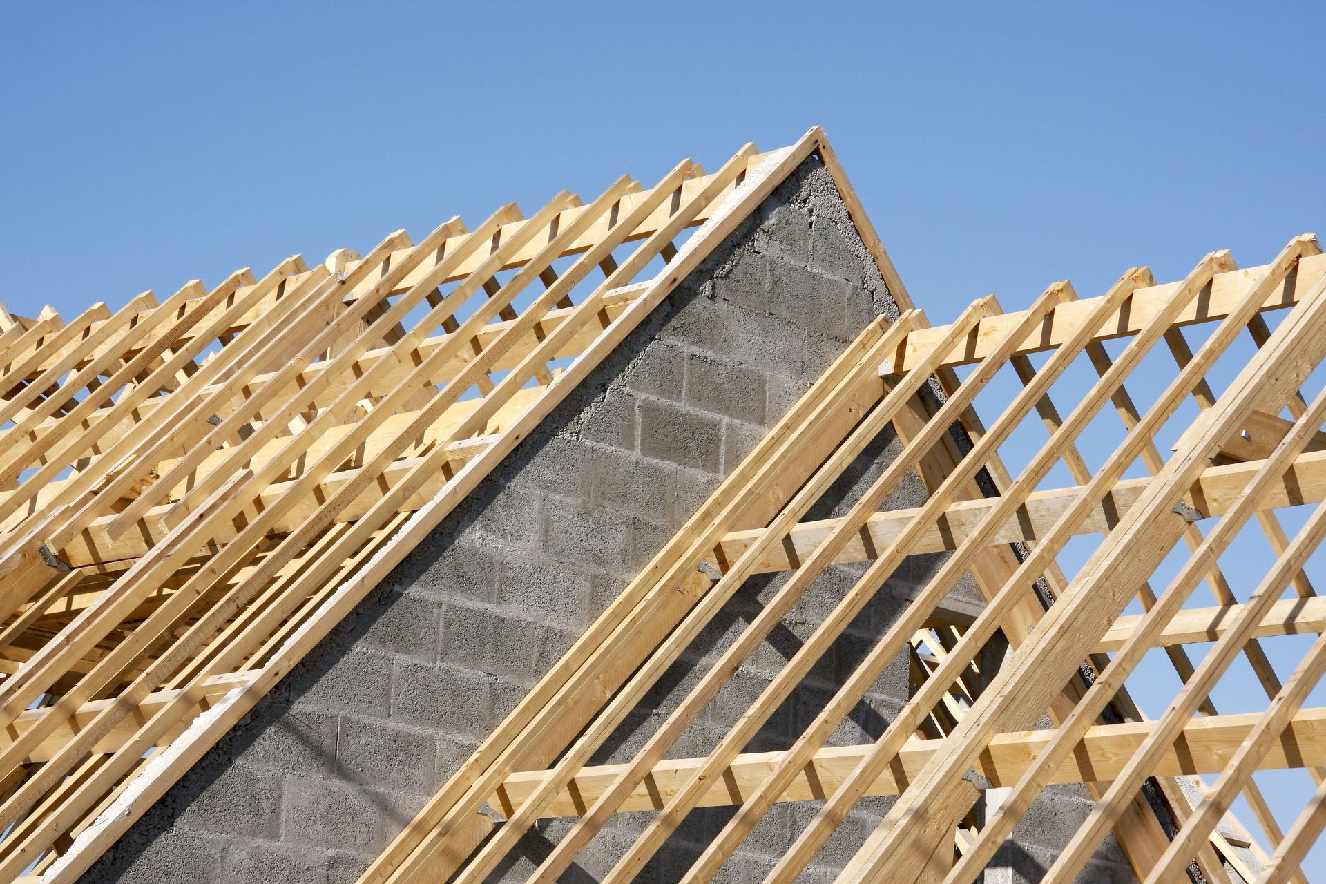 Une charpente de toit en bois en construction, avec ses chevrons se détachant sur un ciel bleu clair.