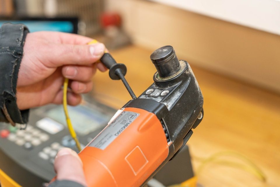Person hält ein orangefarbenes Elektrowerkzeug und testet es mit einer Sonde.