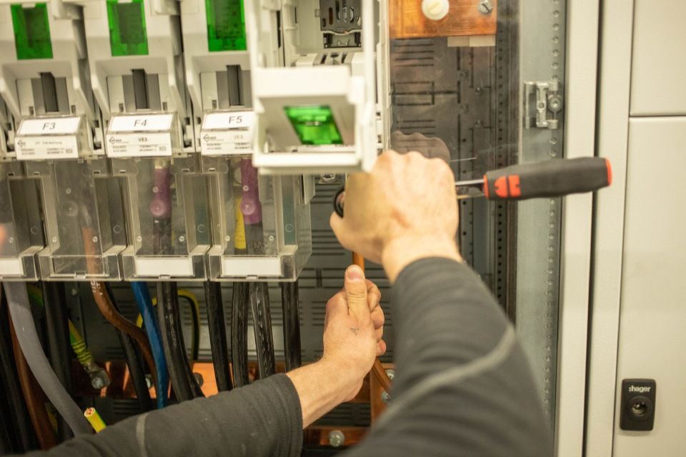 Person arbeitet mit Schraubenzieher an Schalttafel; Drähte sichtbar.
