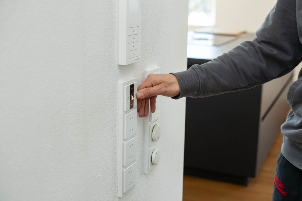 Die Hand einer Person greift nach einem Lichtschalter an einer weißen Wand und betätigt ihn.