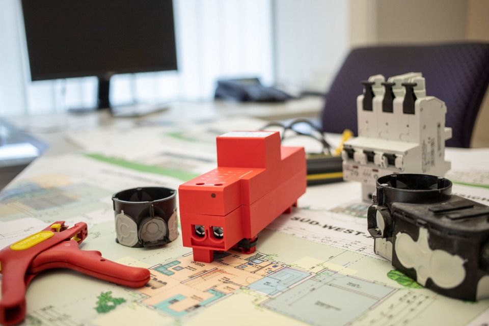 Rote elektrische Komponenten auf einem mit Karten bedeckten Tisch, mit Abisolierzangen und anderen elektrischen Geräten.