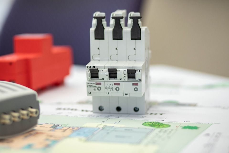 Drei weiße Leistungsschalter auf einer Karte, mit einer roten elektrischen Komponente und einem grauen Gerät in der Nähe.