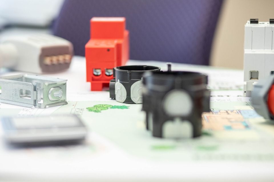 Nahaufnahme verschiedener elektrischer Komponenten, darunter ein roter Überspannungsschutz und schwarze Anschlüsse, auf einem Tisch.