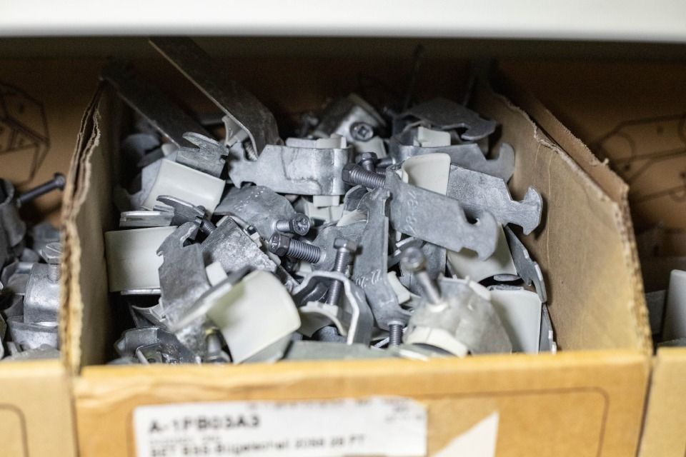 Kartonbehälter gefüllt mit kleinen, grauen und weißen Metall- und Kunststoffteilen.