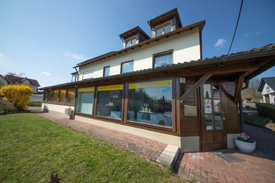 Ein zweistöckiges Gebäude mit einer braunen Holzfassade, Glasfenstern und einem kleinen hölzernen Eingangsbereich unter blauem Himmel.