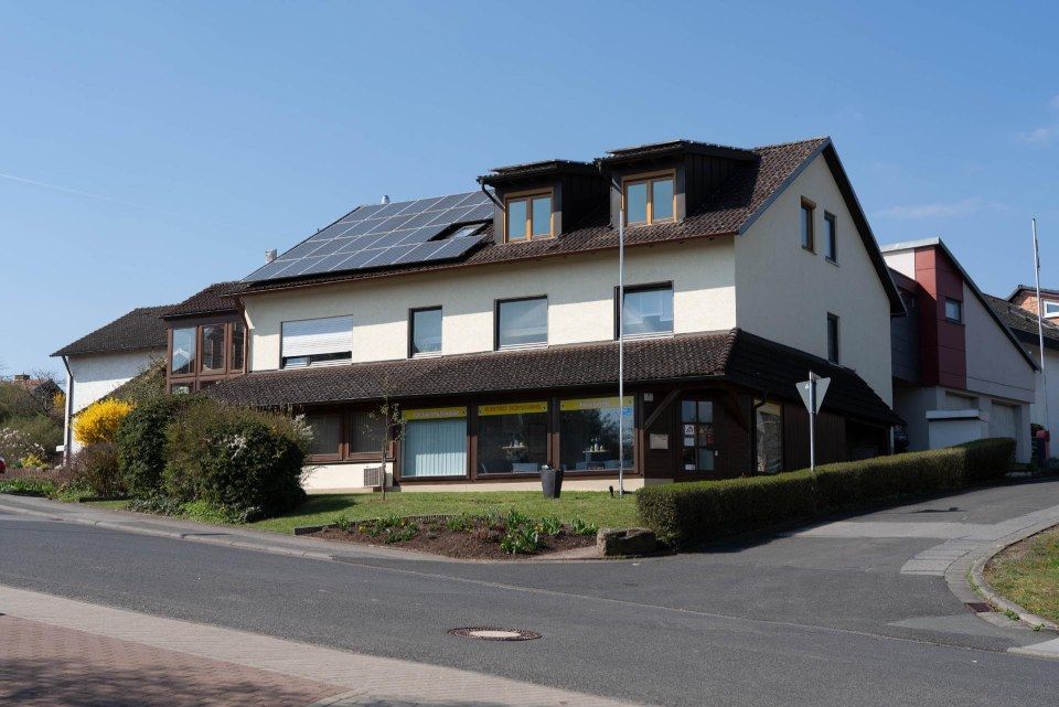 Zweistöckiges Gebäude mit Solarzellen auf dem Dach, in der Nähe einer Straße mit blauem Himmel.