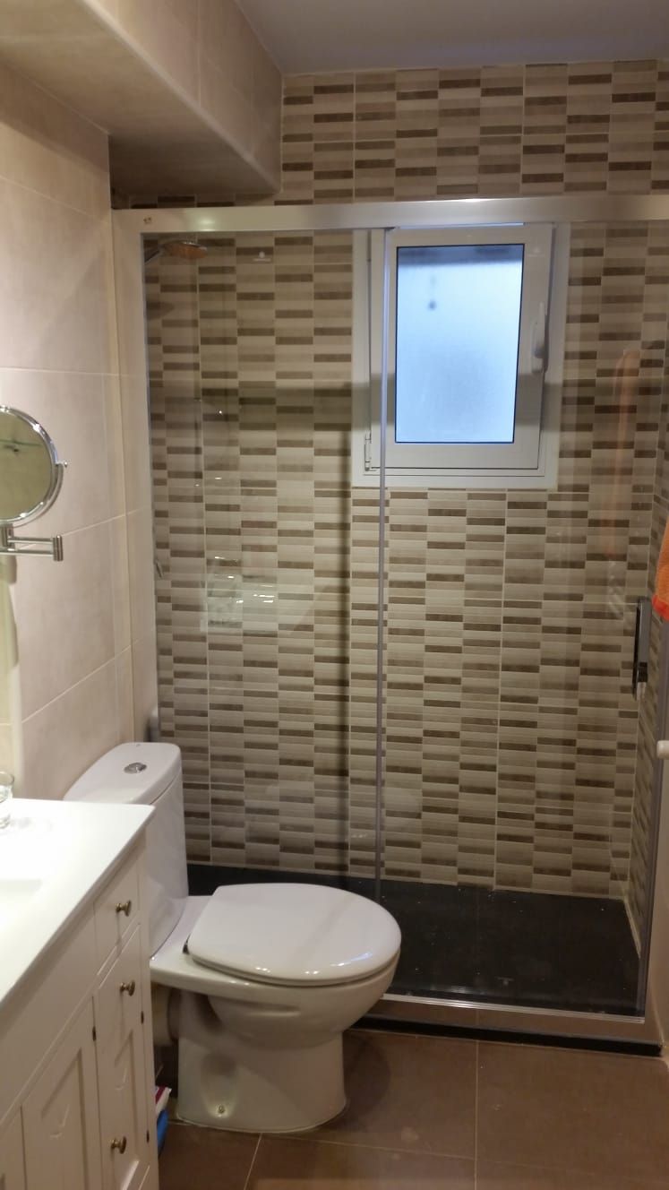 Un baño con inodoro, lavabo, ducha y ventana.