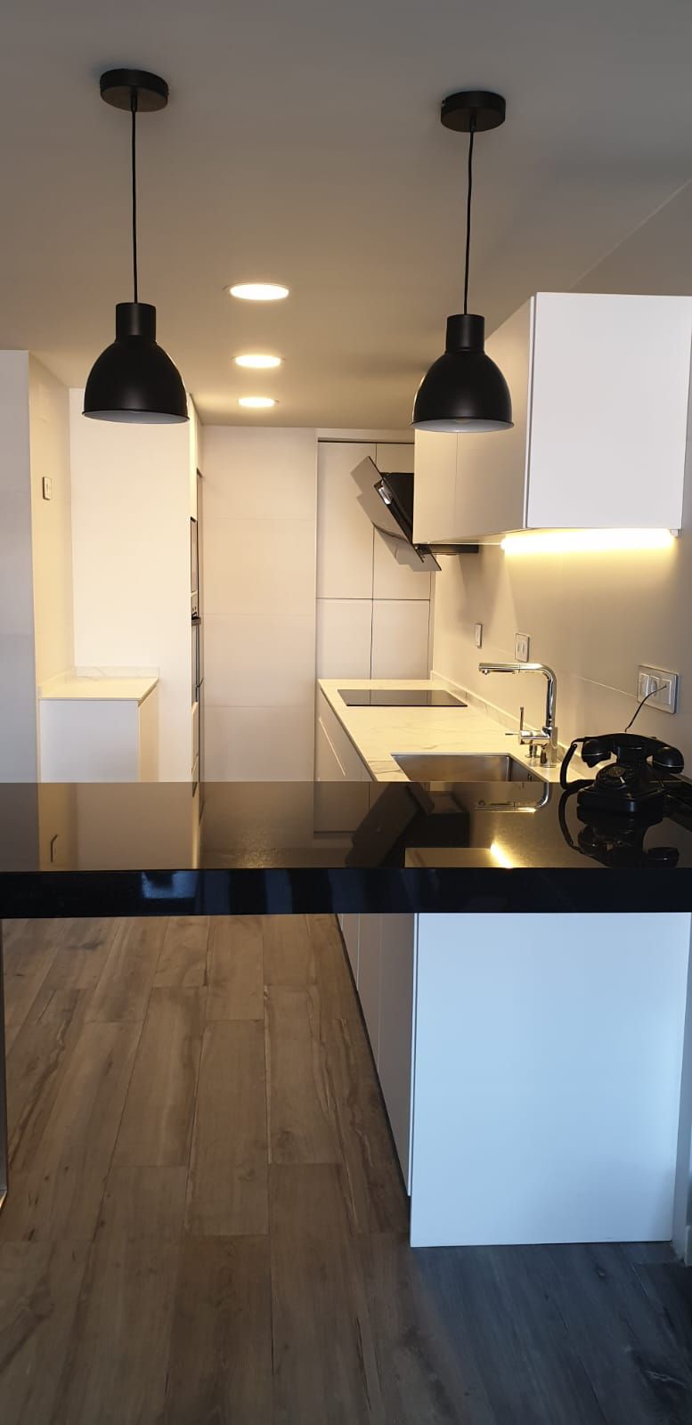 Una cocina con gabinetes blancos, una encimera negra y dos luces colgantes que cuelgan del techo.