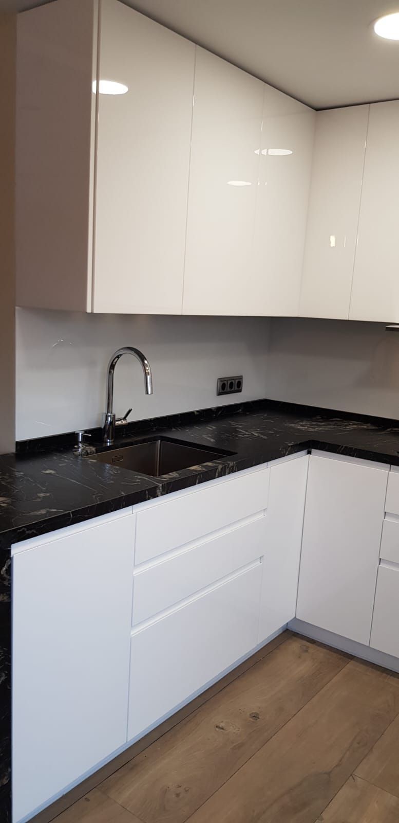 Una cocina con gabinetes blancos, encimeras negras y un fregadero.