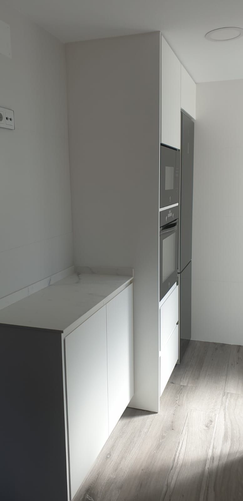 Una cocina con gabinetes blancos, un refrigerador y un microondas.