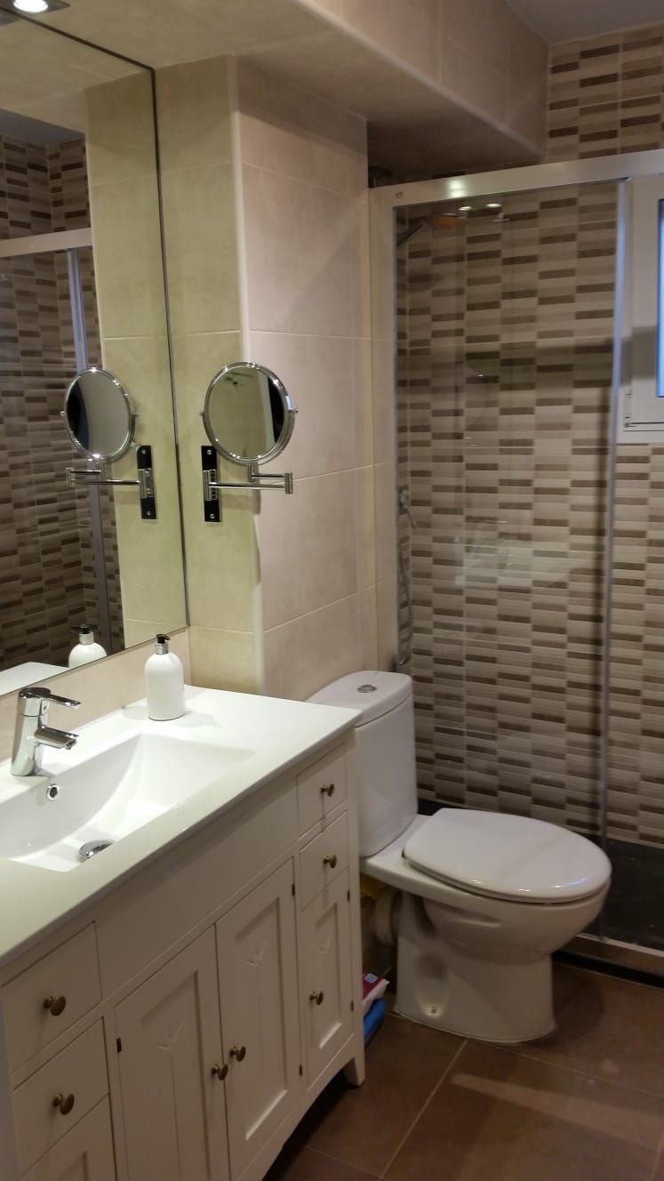 Un baño con inodoro, lavabo, espejo y ducha.