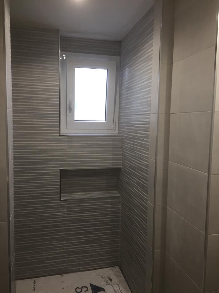 Un baño con una ventana y un estante en la pared.