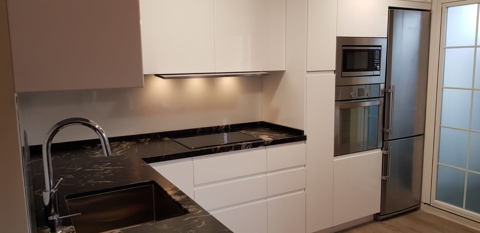 Una cocina con gabinetes blancos, encimeras negras, electrodomésticos de acero inoxidable y un fregadero.