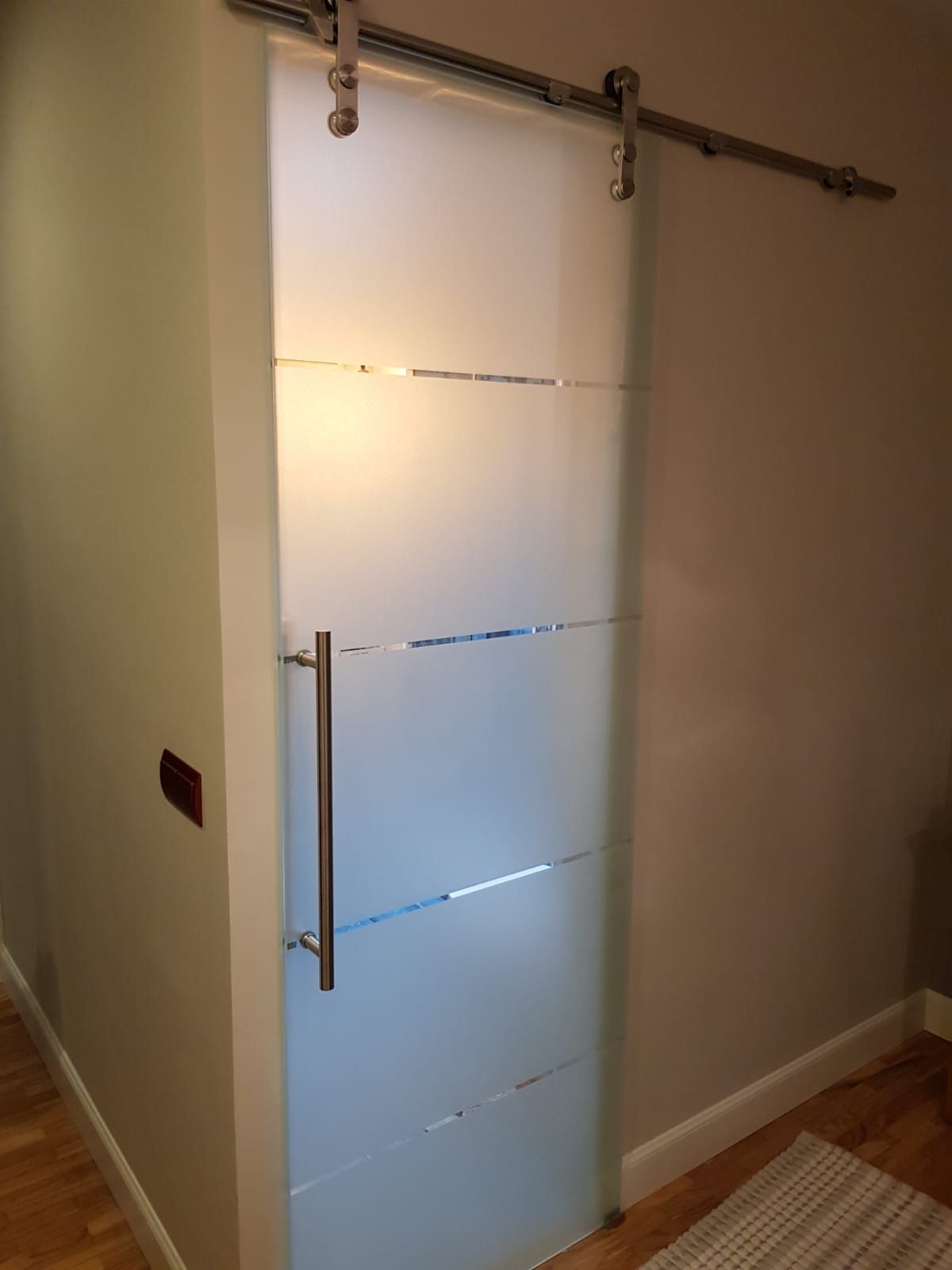 En un pasillo hay una puerta corrediza de vidrio con manija de acero inoxidable.