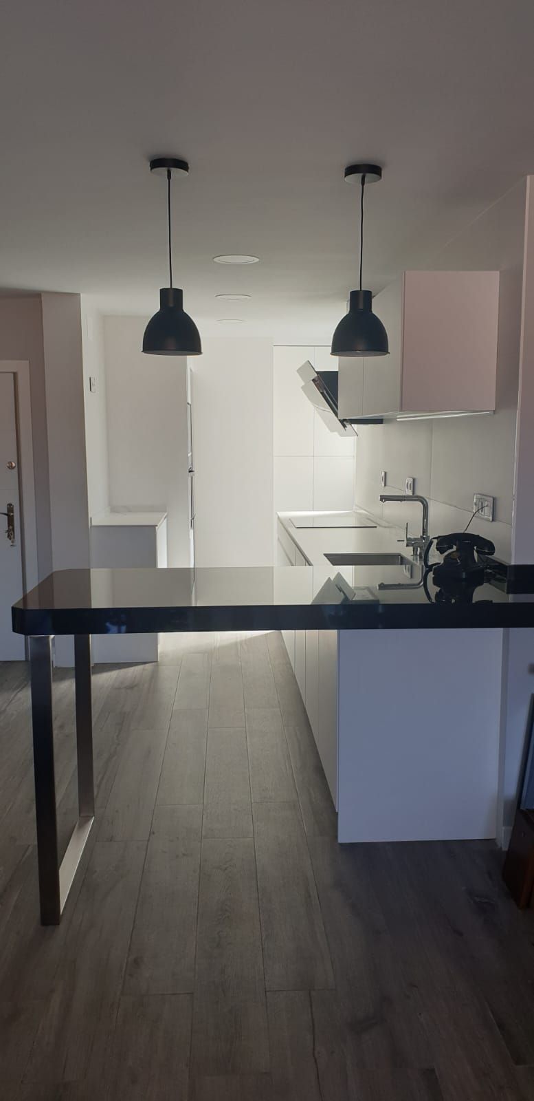 Una cocina con encimera negra y dos lámparas colgantes que cuelgan del techo.