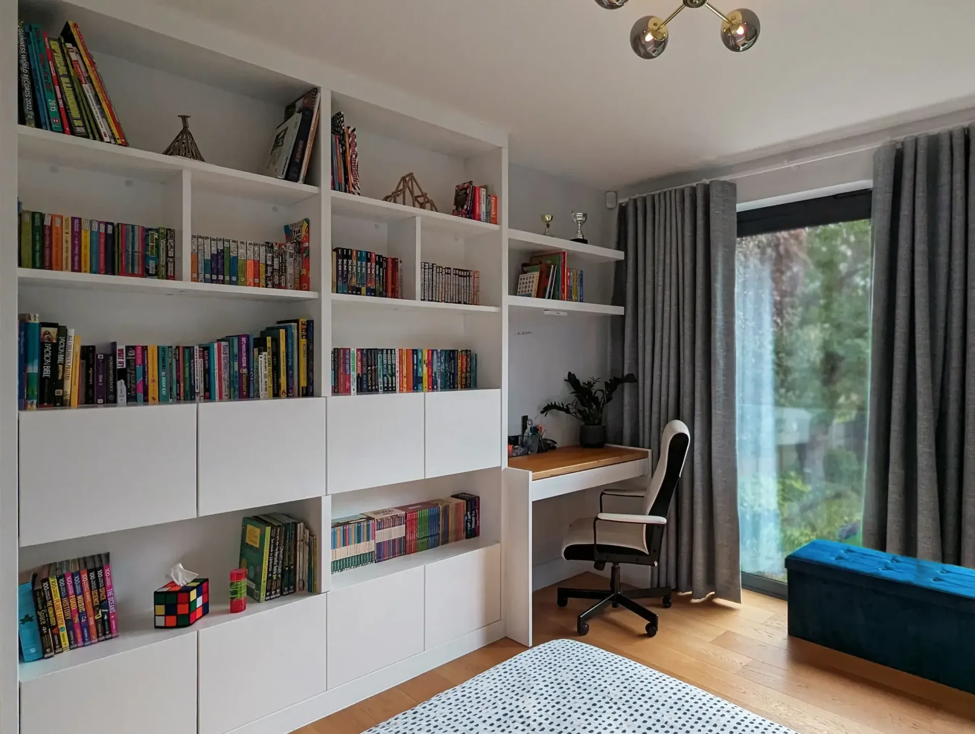 Bright home office with white bookshelves, desk, chair, window, curtains, and blue bench